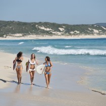 girls-walking-along-beach-with-surfboards